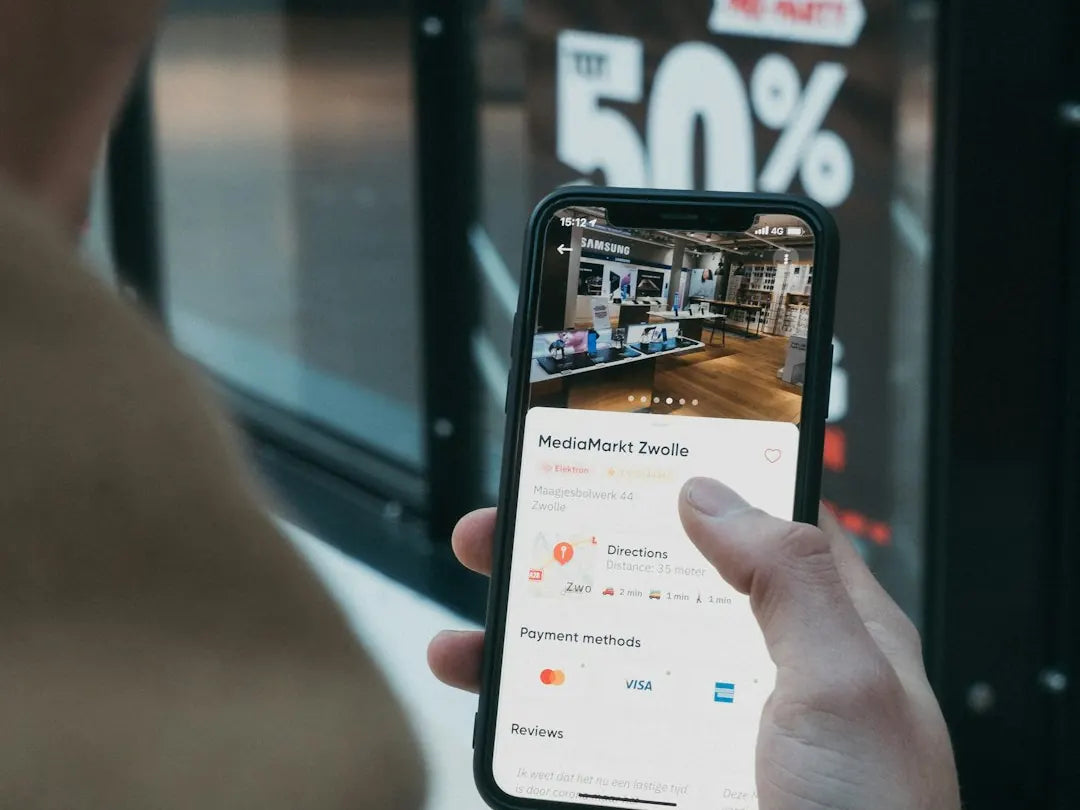 A hand holding a phone showing a store page with directions and payment methods