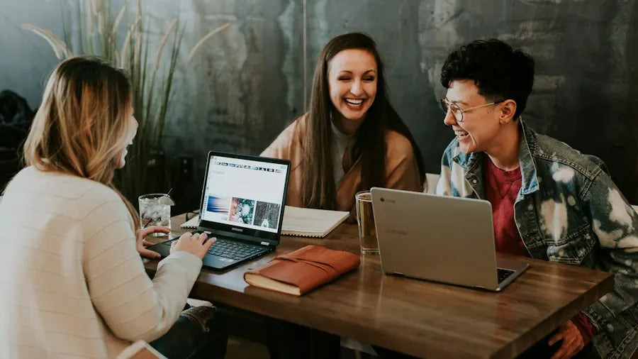 Three Bristm team members laughing together around a laptop at a wooden table